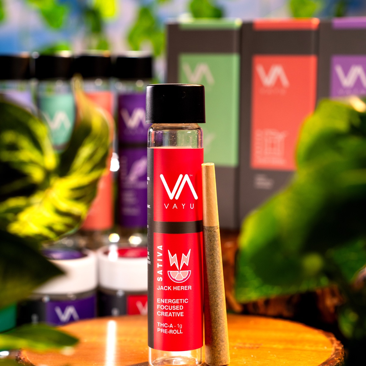 Red-labeled VAYU cannabis vape cartridge with a pre-roll beside it on a wooden table, colorful packaging in the blurred background.